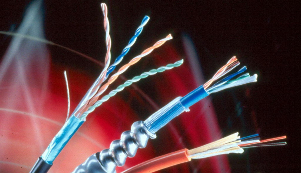 Różne typy kabli sieciowych, w tym kabel światłowodowy z metalową osłoną spiralną, kabel UTP z odsłoniętymi skrętkami oraz kabel koncentryczny, na abstrakcyjnym czerwono-czarnym tle.